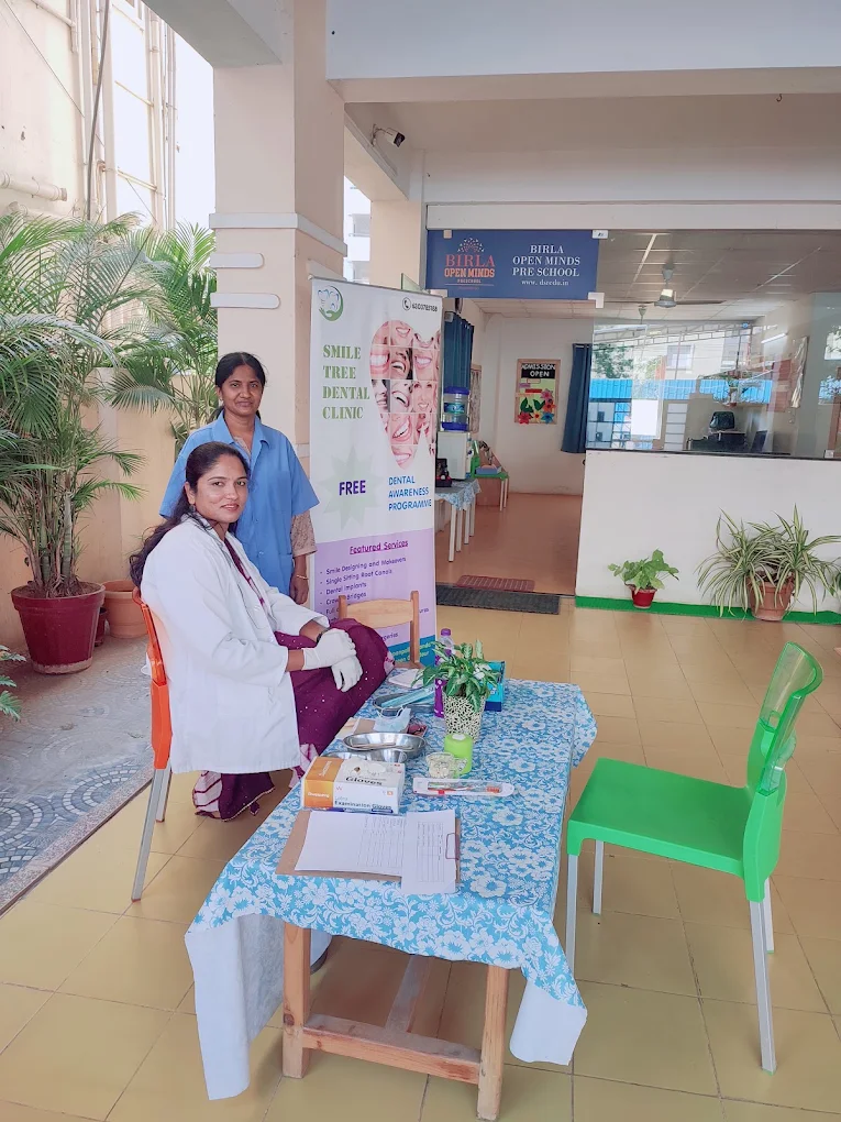 Two people seated at a Smile Tree Dental Clinic information table near the clinic entrance.